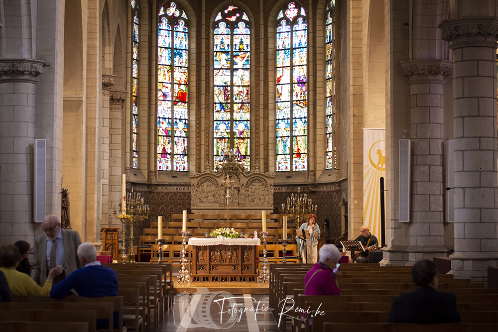 Kerkinterieur met glas-in-loodramen, altaar en muzikanten.