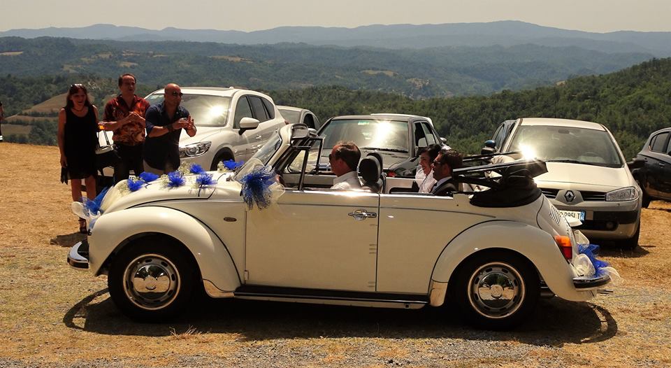 Witte vintage cabriolet trouwauto met gasten, versierd met blauwe bloemen, een leuke trouwdag