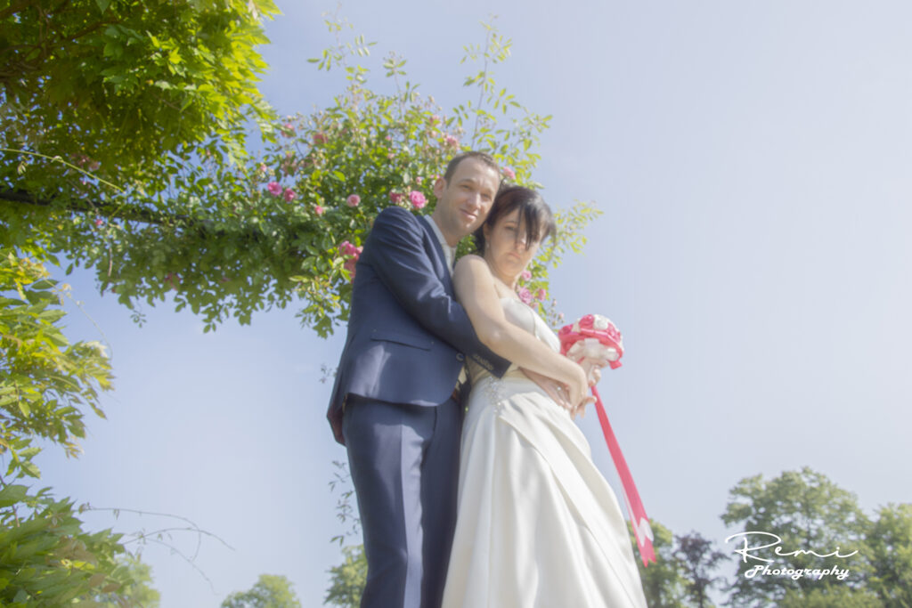 Jonggehuwden omhelzen elkaar onder een bloemenboog, huwelijk in Niel