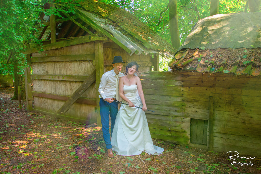 Het pasgetrouwde stel poseert voor een foto tijdens hun bruiloft in Niel, voor een oud houten gebouw.