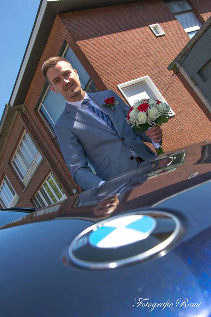 Bruidegom bij een huwelijk Strijboshof Kalmthout, met bloemen naast een auto.