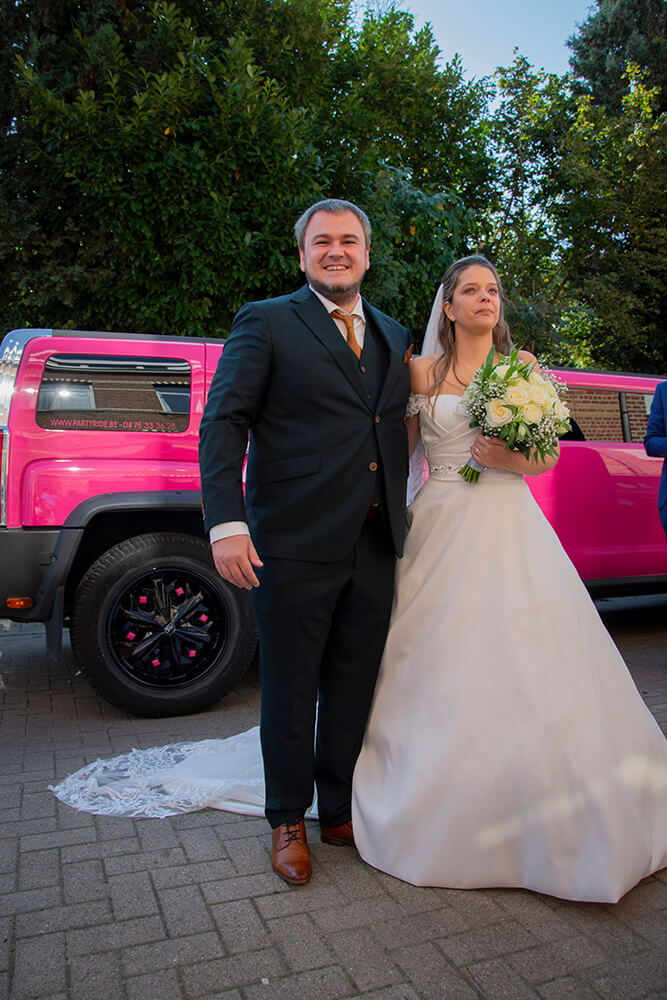 Pasgetrouwd stel poseert naast een roze Hummer-limousine, bruiloft in Boom.