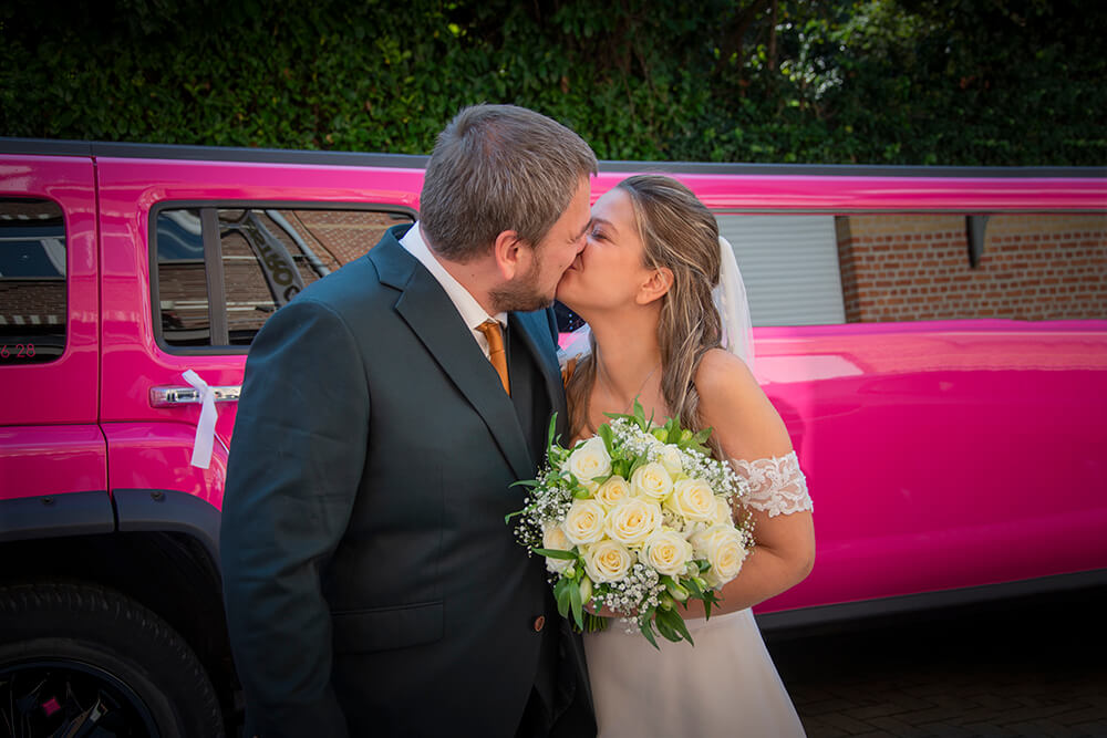 Pasgetrouwden delen een tedere kus naast een roze bruidslimousine. Het bruidspaar viert hun speciale dag.