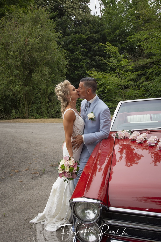 Jonggehuwden delen een kus naast een klassieke rode auto; 2-daagse-huwelijksreportage