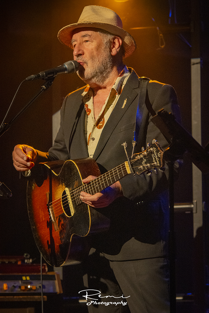 Muzikant op het podium die een vintage Recording King-gitaar bespeelt, livemuziekfotografie.