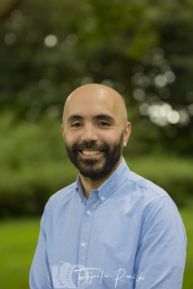 Kale man met een baard, lachend tegen een groene achtergrond.