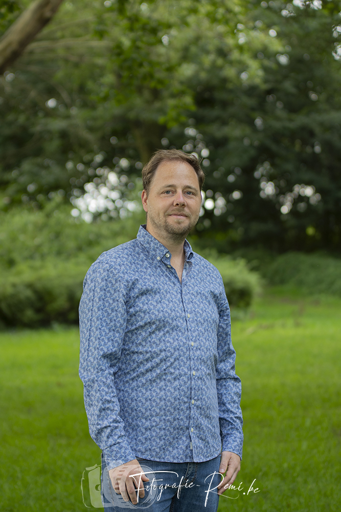 Man in een blauw gebloemd overhemd staand in een park