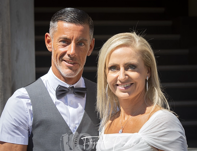 Koppel glimlachend voor een 2-daagse-huwelijksreportage. Man in vest, vrouw in witte jurk.