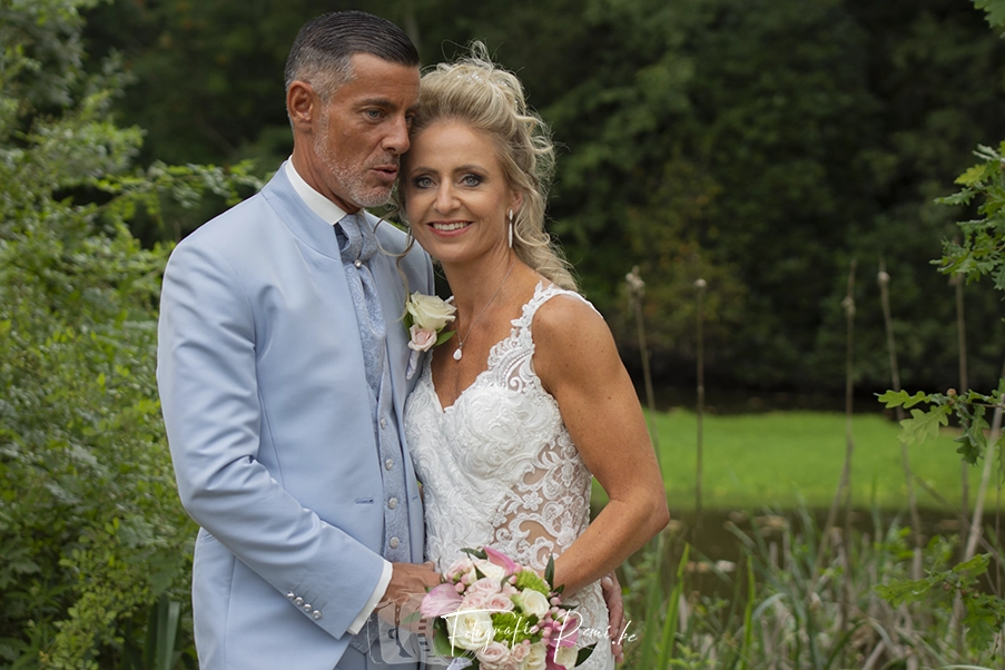 Jonggehuwden omhelzen elkaar tijdens een 2-daagse-huwelijksreportage. Bruid in kanten jurk, bruidegom in blauw pak.