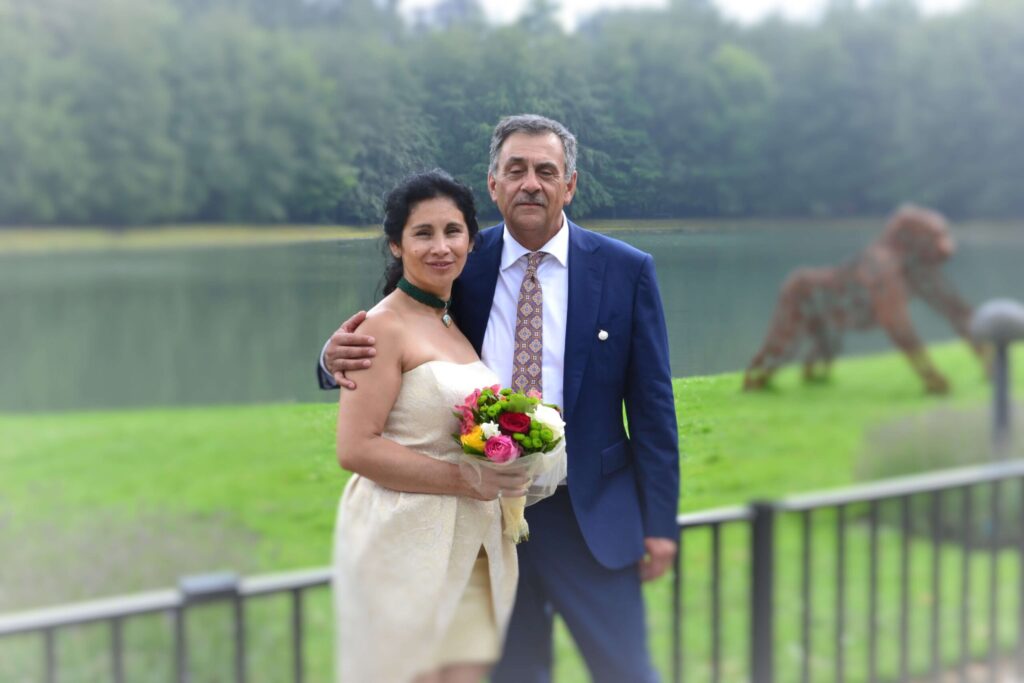 Het pasgetrouwde stel poseert voor een portret buiten, met het meer en het groen op de achtergrond.