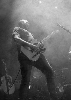 Kale gitarist speelt op het podium met een Fender Telecaster, met podiumverlichting en rook, livemuziekfotografie